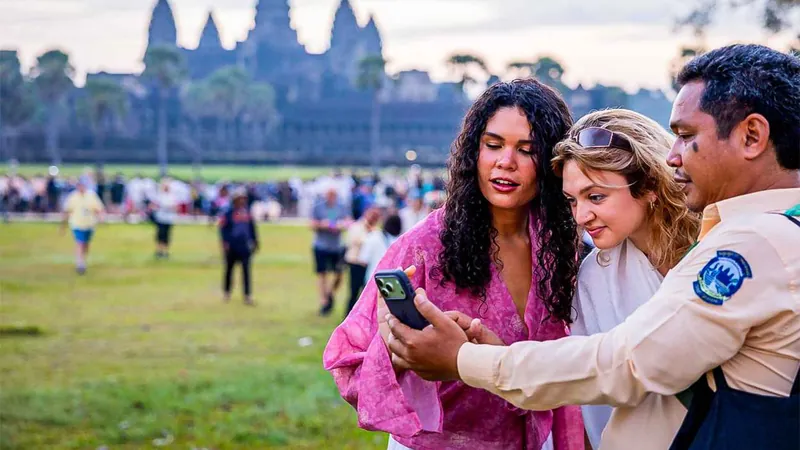 A guide showing two travelers a photo on a phone in front of the Angkor Wat towers at dawn on a small-group Angkor Wat tour from Siem Reap