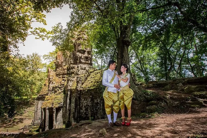 A couple in traditional Khmer costume beside a ruined temple gate under tall trees on a three-day Angkor Wat tour