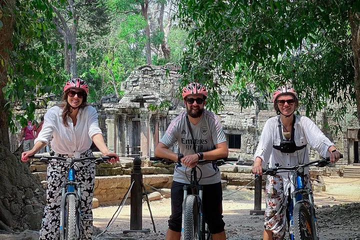 Three cyclists posing with their bikes in front of a temple ruin on an Angkor sunrise cycling tour