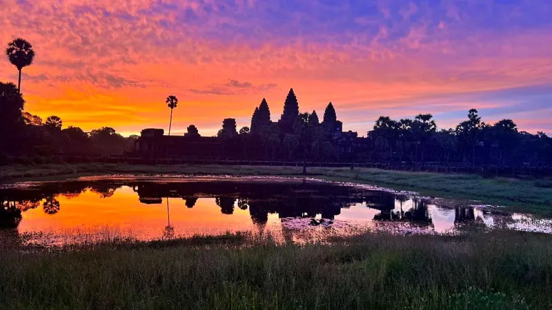 Angkor Wat towers silhouetted against a purple and orange sunrise over the reflecting pond on an Angkor Wat sunrise tour