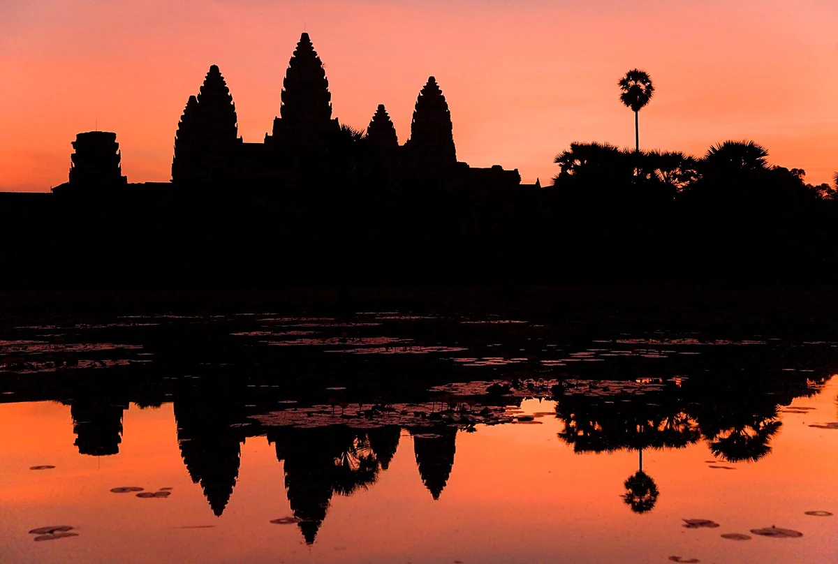 Angkor Wat silhouetted against an orange dawn sky and reflected in the pond, seen on Angkor Wat tours from Siem Reap