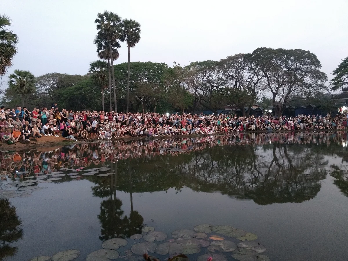 Visitors lining the edge of the reflecting pond in the dim light before sunrise at Angkor Wat, the first stop on Angkor Wat sunrise tours