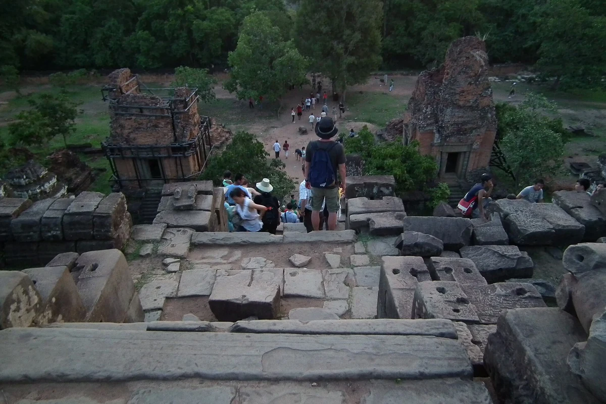 Visitors on the stone terraces of the Phnom Bakheng summit looking out over the forest, seen on Angkor Wat tours from Siem Reap