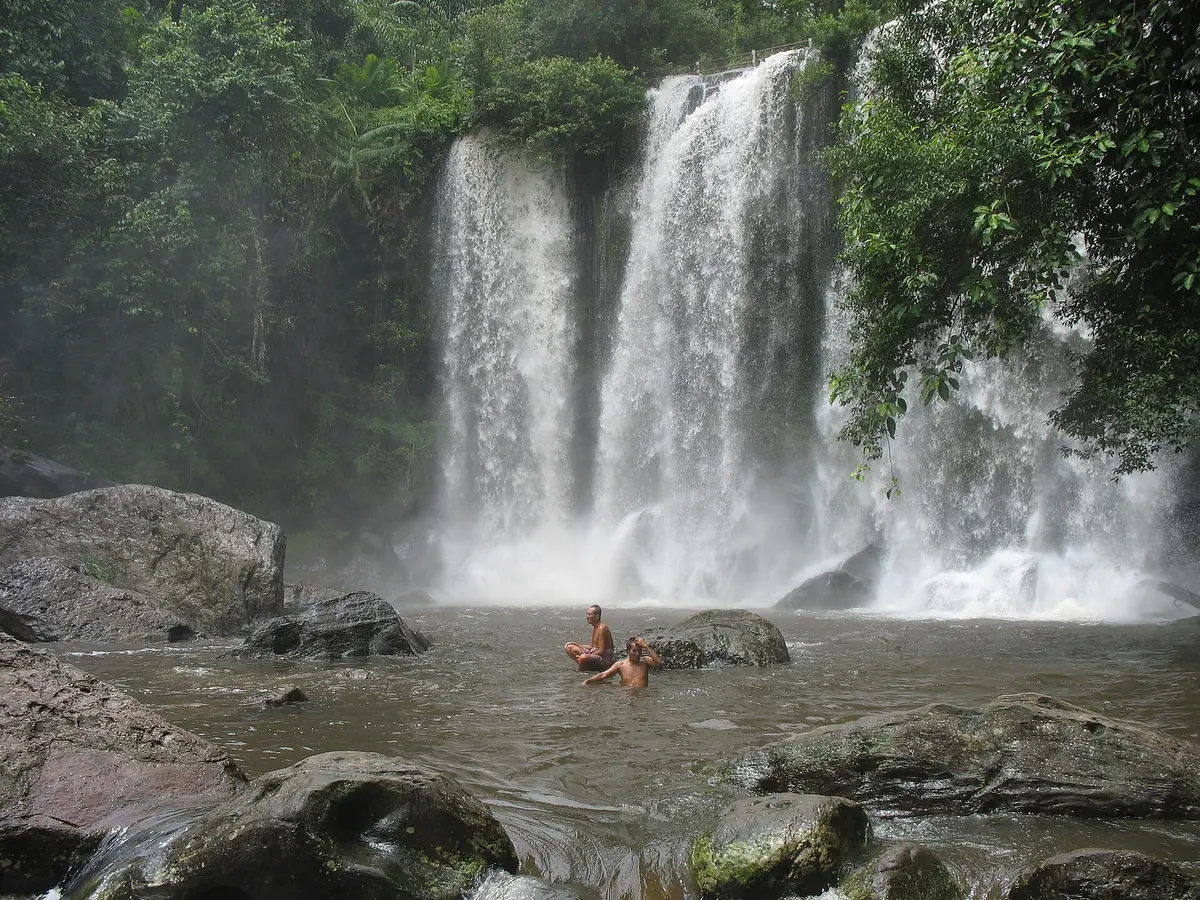 A two-stream waterfall on Phnom Kulen with swimmers in the pool below, seen on Angkor Wat tours from Siem Reap